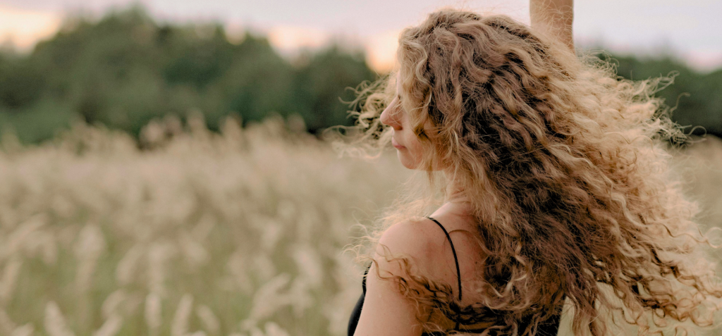 Frau mit lockigem Haar tanzt auf einem Feld in der Natur. Sie strahlt ein Gef&uuml;hl von Freiheit aus.