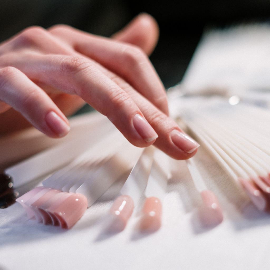 Hand mit nude N&auml;geln &uuml;ber einer Reihe von Nagelmustern, Trainee Treatments in Basel.