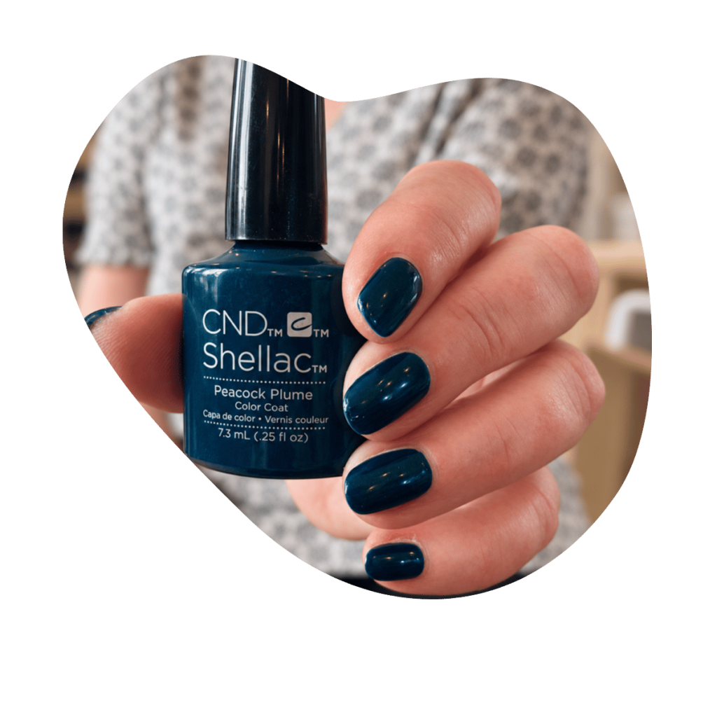 Hand mit dunkelblau lackierten N&auml;geln h&auml;lt CND Shellac Peacock Plume Flasche, TPO frei und HEMA frei, Beautylounge Basel.