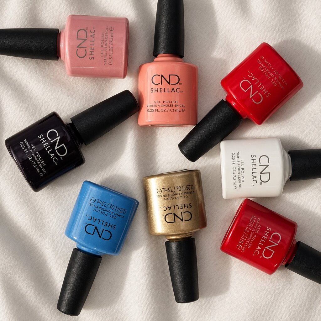 Acht CND Shellac Gel Polish Flaschen in Rosa, Koralle, Rot, Blau, Gold und Weiss auf hellem Stoff, Beautylounge Basel.