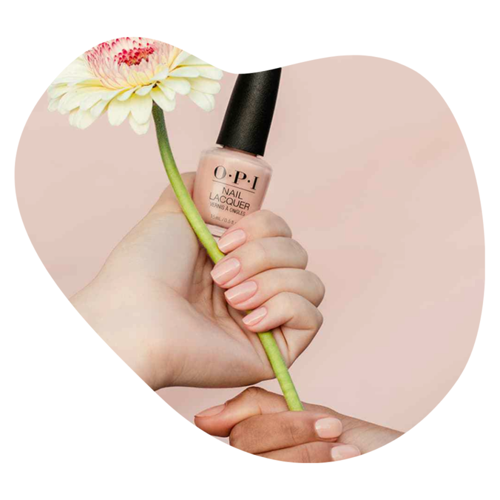 Hand h&auml;lt eine O.P.I Nagellackflasche neben einer Blume, Farbauswahl f&uuml;r die Manicure bei Beautylounge Basel.