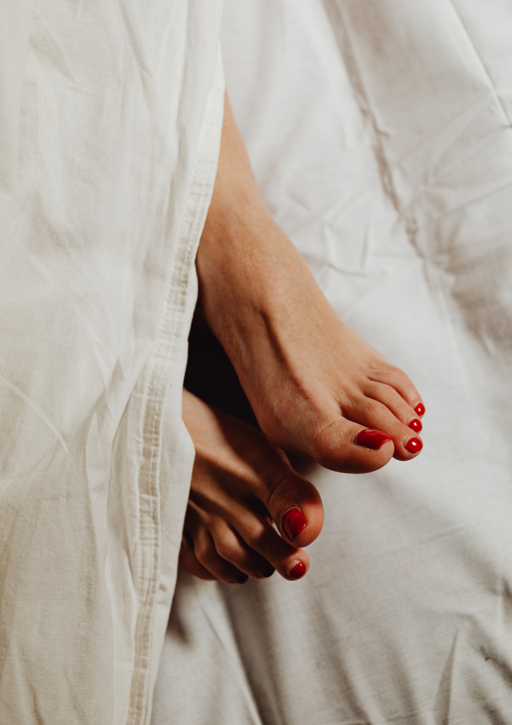 F&uuml;sse mit rot lackierten Zehenn&auml;geln auf hellem Bettzeug nach einer Pedicure in Basel.