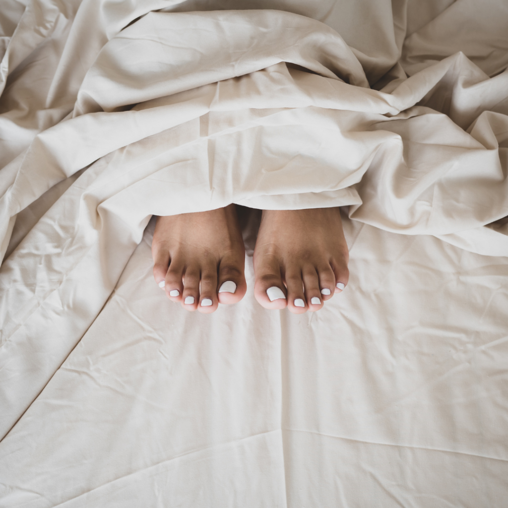 Gepflegte F&uuml;sse mit weiss lackierten Zehenn&auml;geln auf hellem Bettzeug nach einer Pedicure.