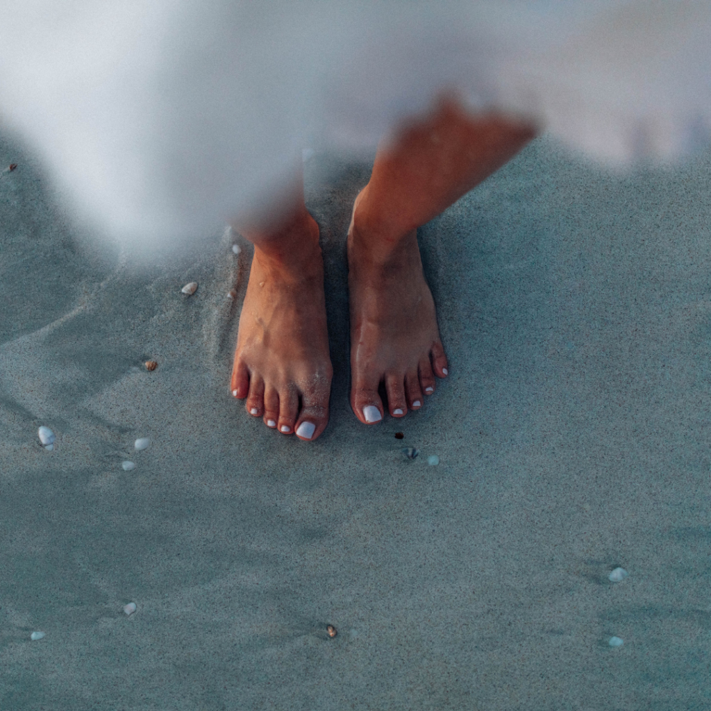 Gepflegte F&uuml;sse mit weiss lackierten Zehenn&auml;geln im nassen Sand am Strand nach einer Pedicure.